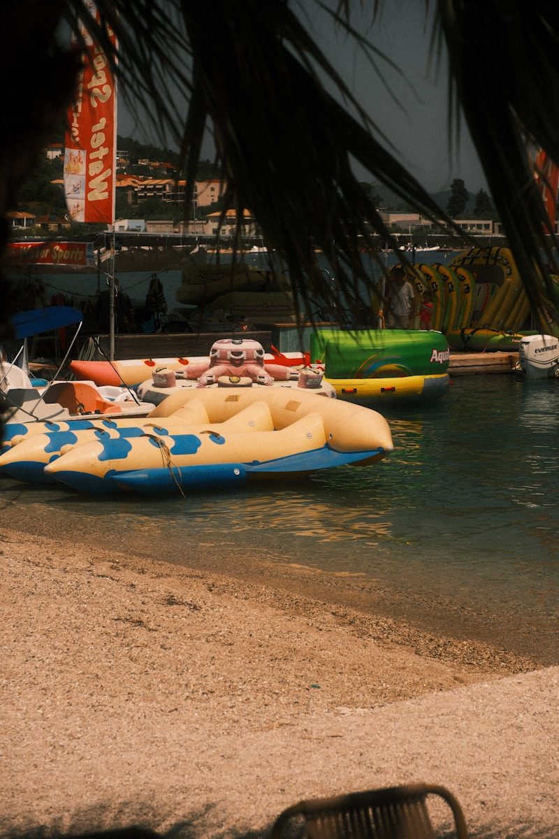 Inflatable water sports equipment moored at a sandy beach near a pier